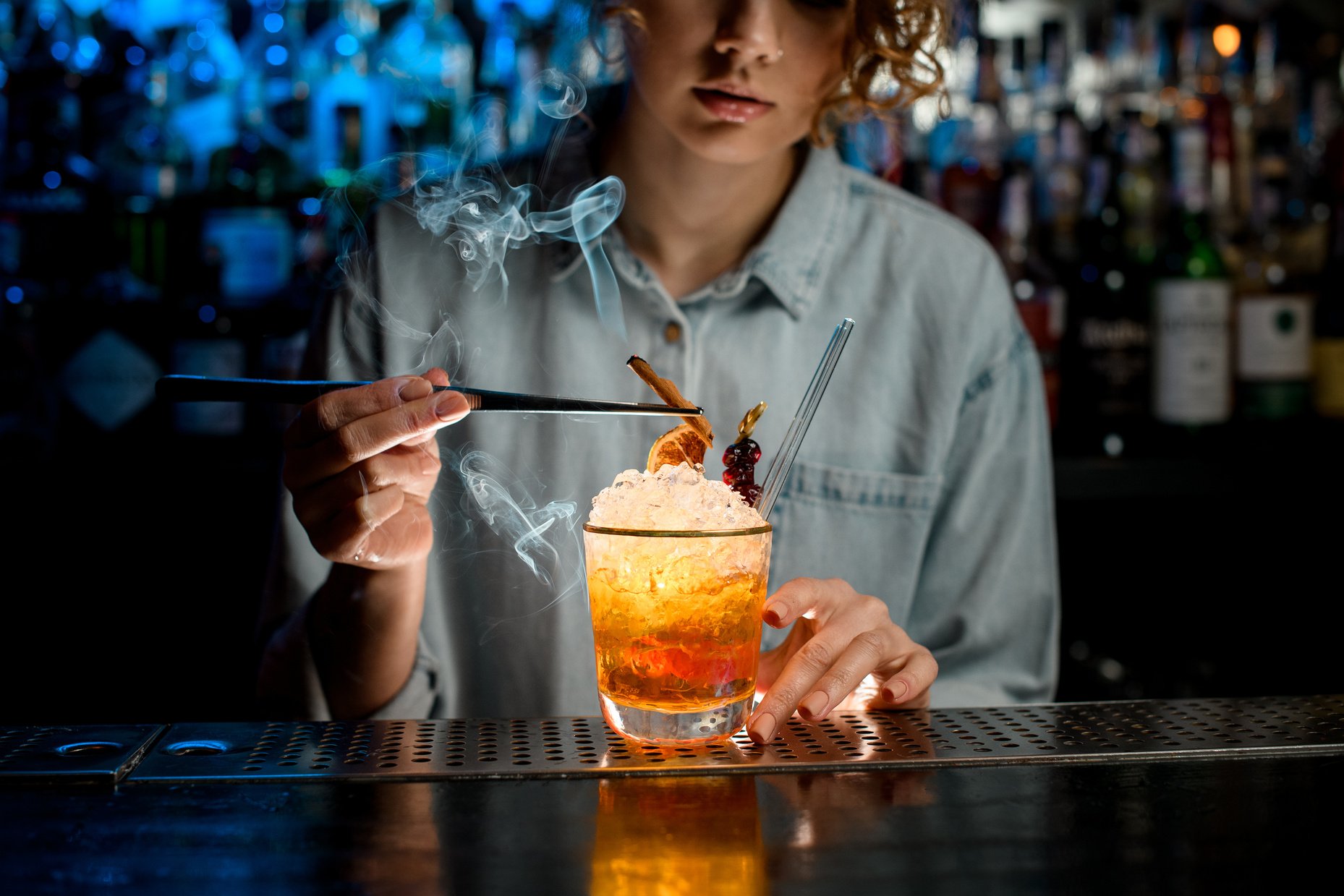 Lady bartender decorates bright cocktail like negroni using tweezers.